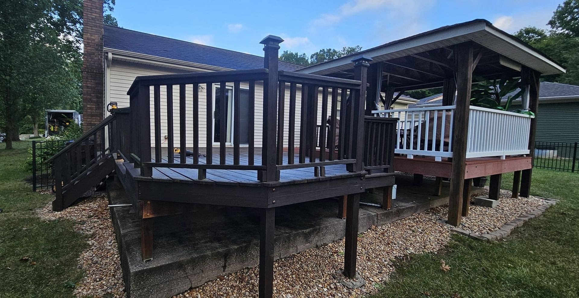 Wooden deck with railings and covered patio on a gravel yard beside a house
