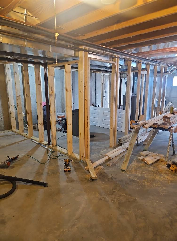Unfinished basement with exposed wooden framing, insulation, and construction tools on a concrete floor