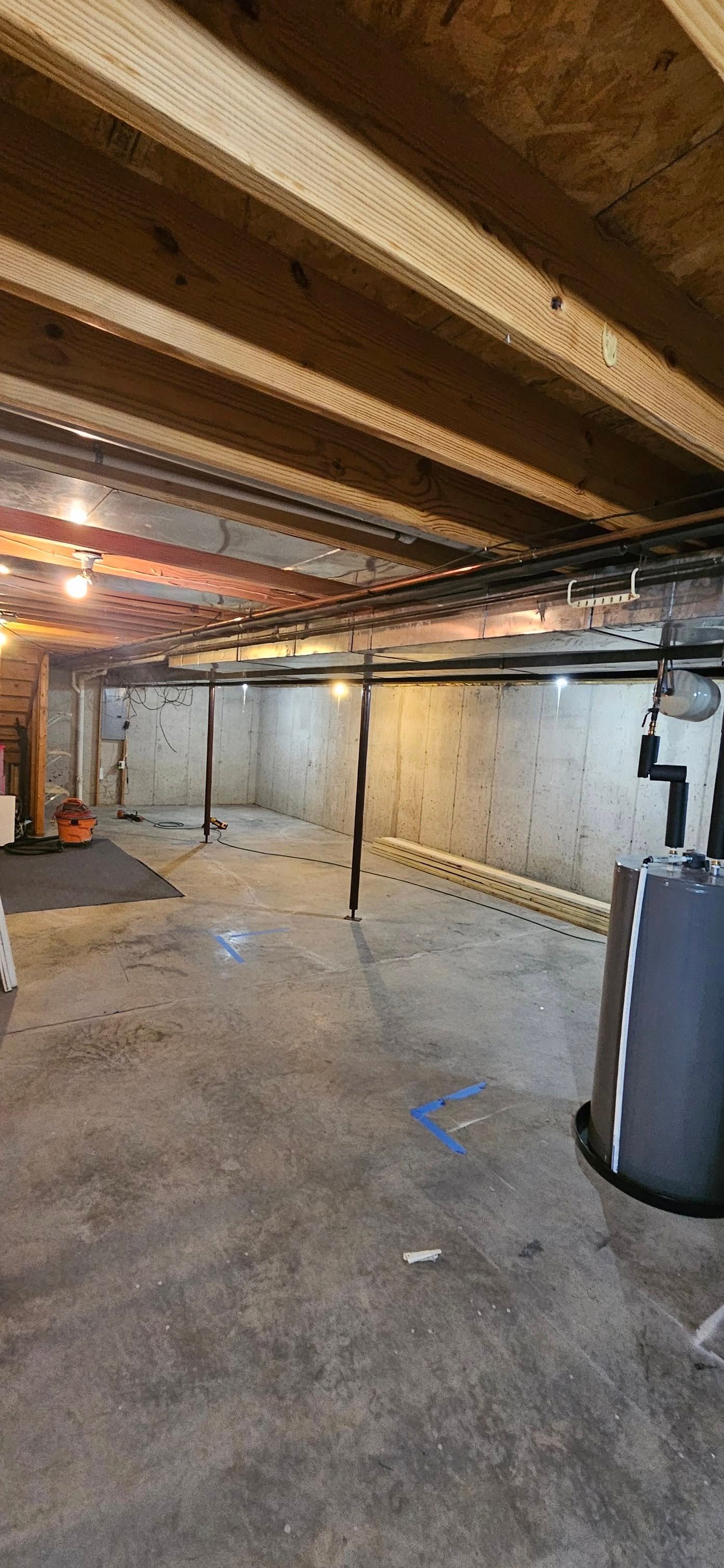 Unfinished basement with exposed beams, concrete floor, and utility equipment against the walls