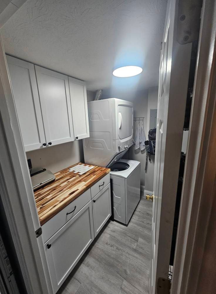 Narrow galley kitchen with white cabinets, wood countertop, washer-dryer, and ceiling light