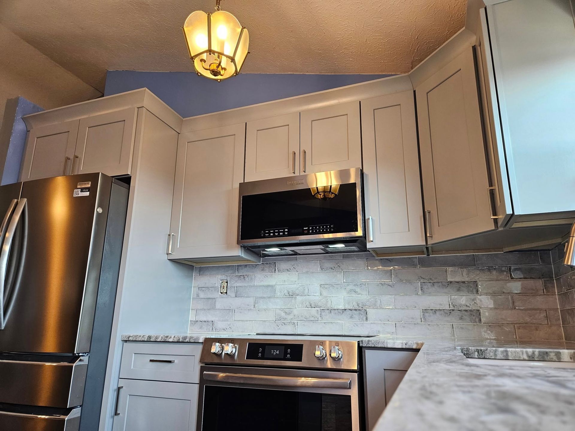 Modern kitchen corner with gray cabinets, stainless appliances, white tile backsplash, and a hanging ceiling light