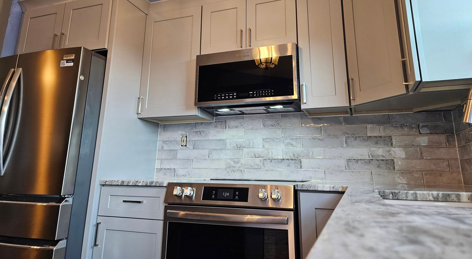 Modern kitchen with stainless steel refrigerator, stove, range hood, white cabinets, and gray tile backsplash