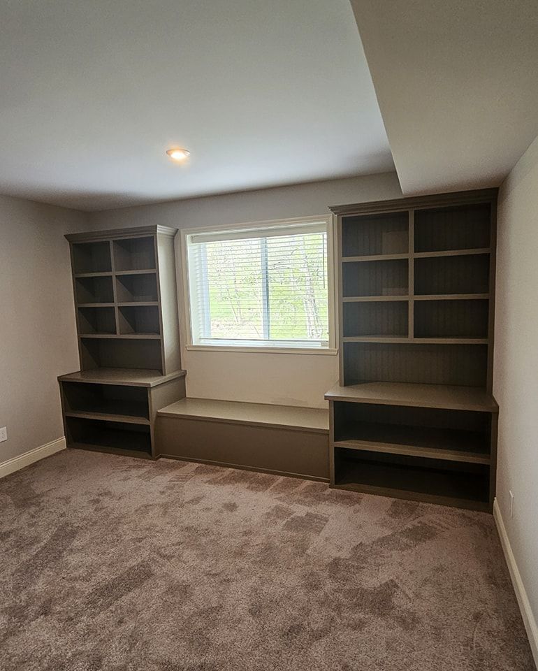 Built-in shelves and window seat in a carpeted room with a window and gray walls