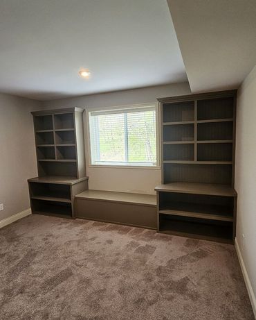 Built-in shelves and window seat in a carpeted room with a window and gray walls