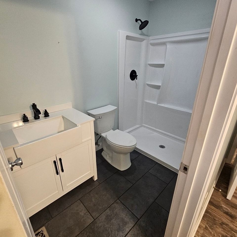 Small bathroom with white vanity, toilet, black tile floor, and walk-in shower.