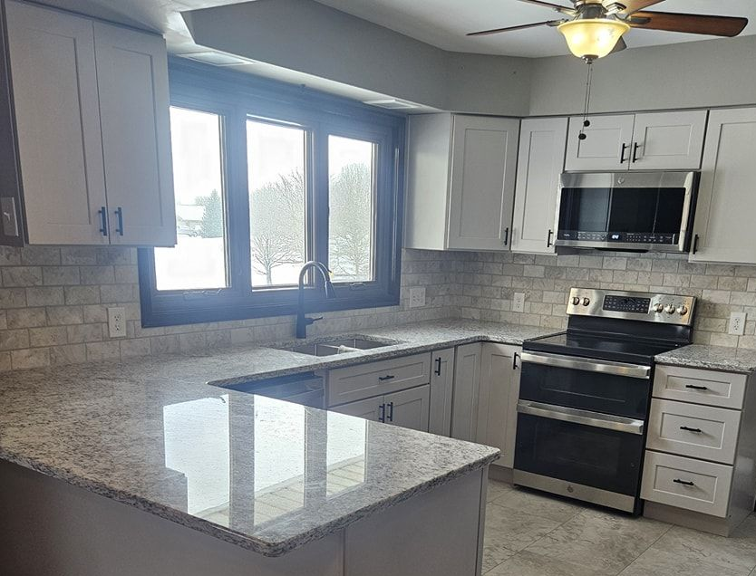 Modern kitchen with gray cabinets, granite counters, stainless steel appliances, and a window over the sink