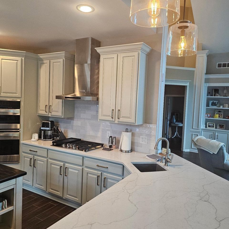 Bright modern kitchen with white cabinets, marble island, stainless range hood, and pendant lights