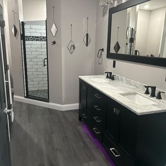 Modern bathroom with double vanity, large mirror, dark cabinets, gray flooring, and tiled shower.