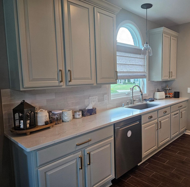 Bright kitchen with white cabinets, gray countertops, arched window, and dark dishwasher.