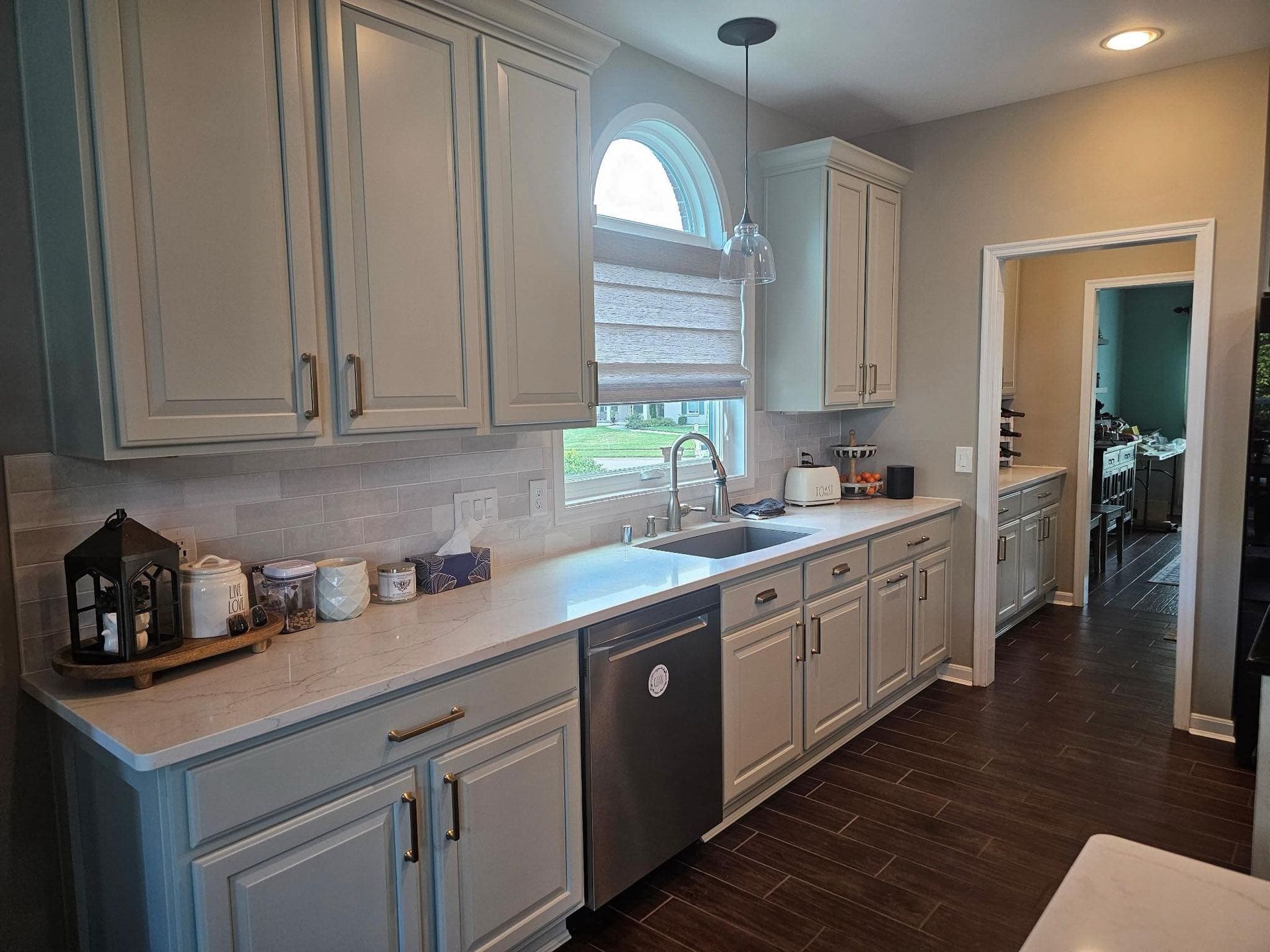 Modern kitchen with gray cabinets, dark wood floor, stainless dishwasher, and window over the sink