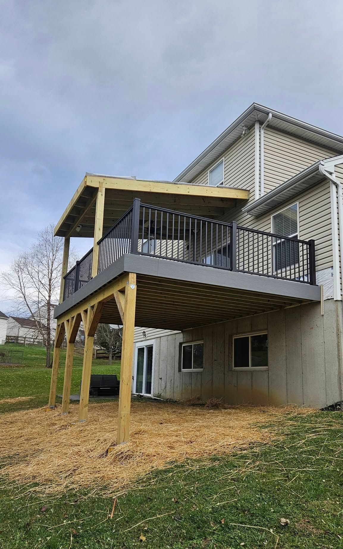 Raised wooden deck and covered porch attached to a beige house on a grassy hillside.
