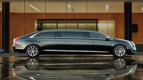 A long black limousine is parked in front of a building.