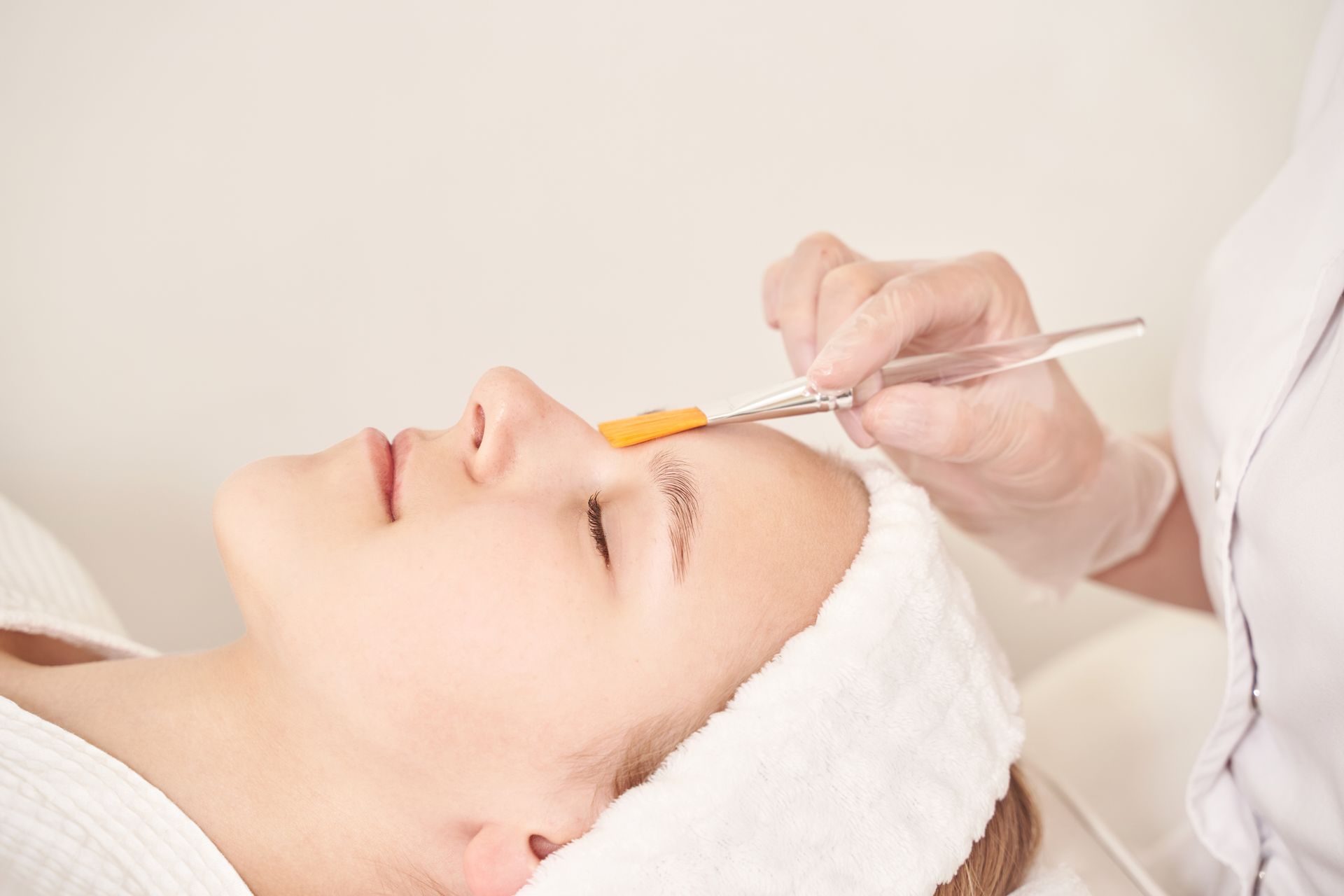 Cosmetician applying a facial treatment with a brush to a client lying on a spa bed