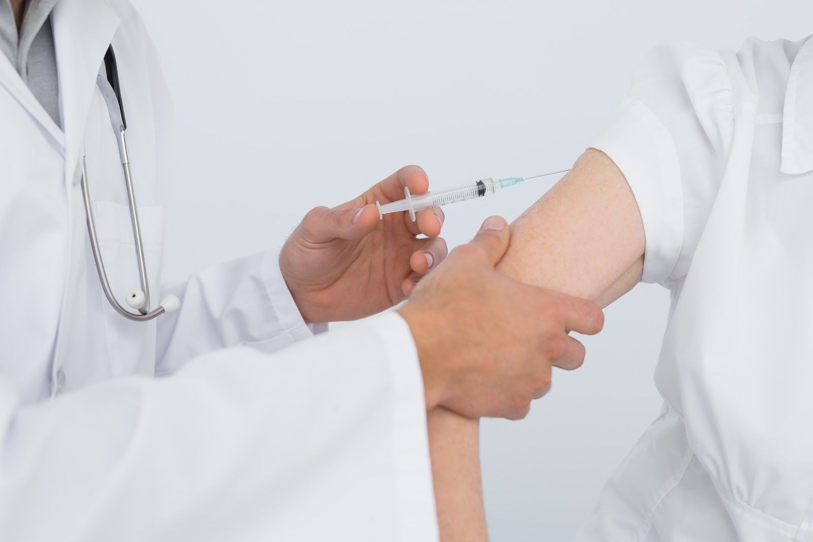 Doctor giving an injection to a patient's upper arm in a white clinical setting