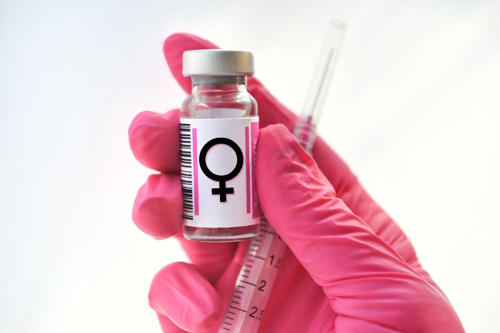Gloved hand holding a vial with female symbol, with a syringe in the background