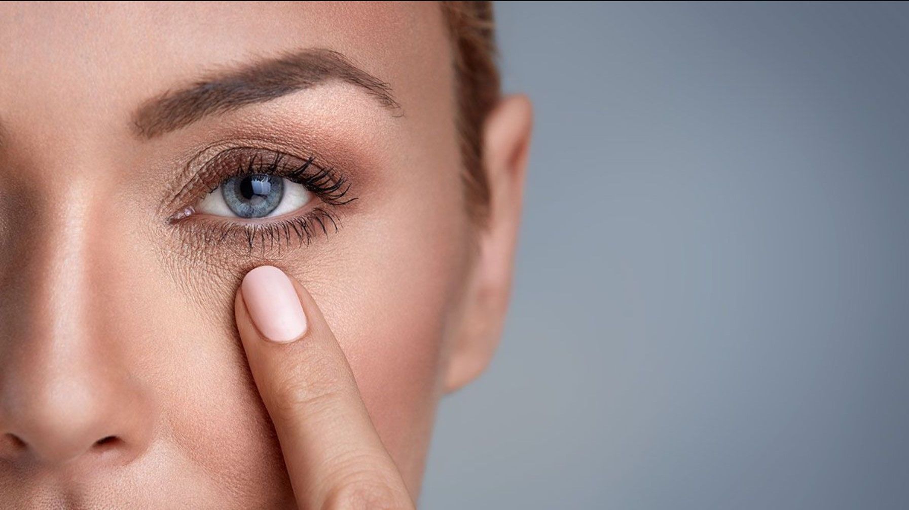 A woman is applying lotion to her face with her eyes closed.