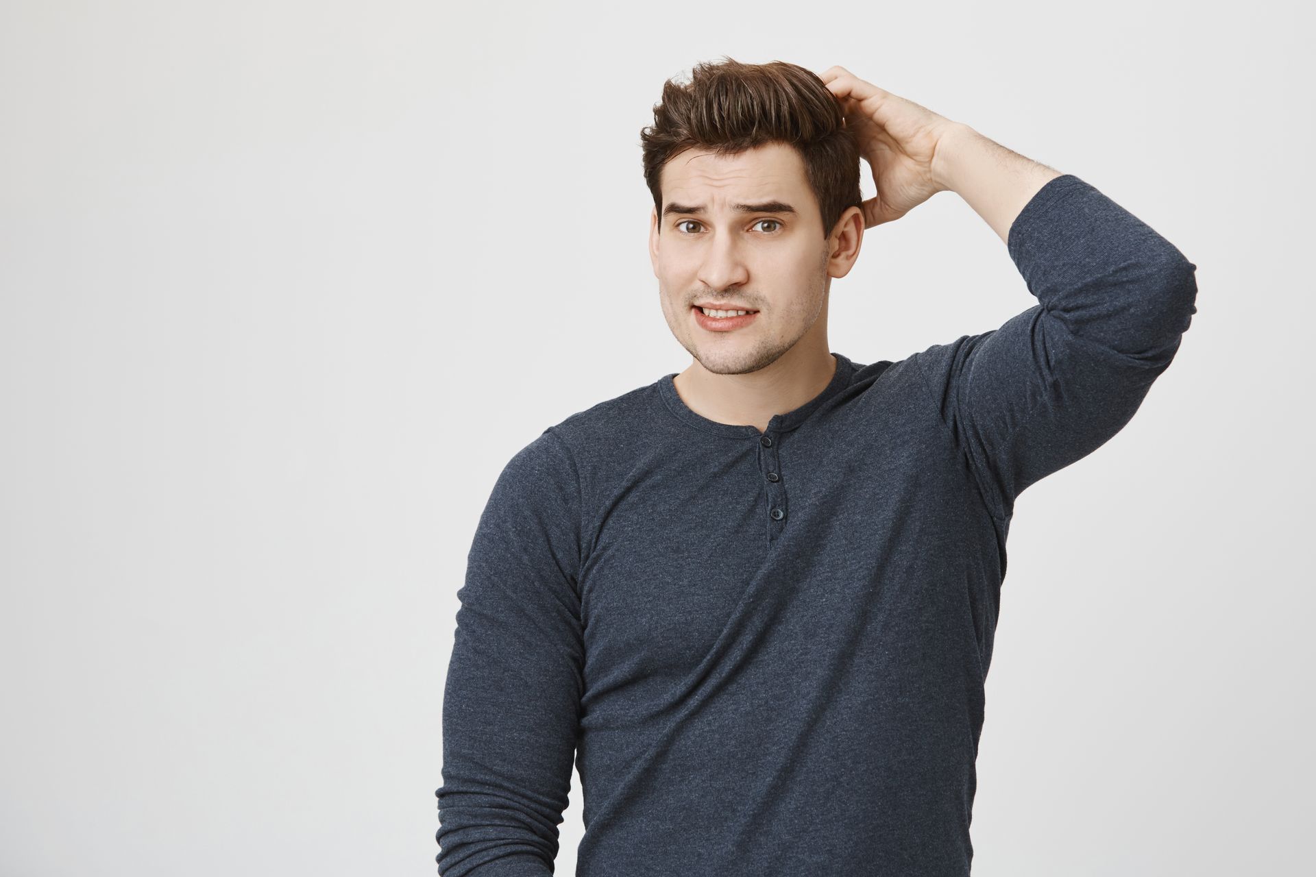 A man in a blue shirt is scratching his head.