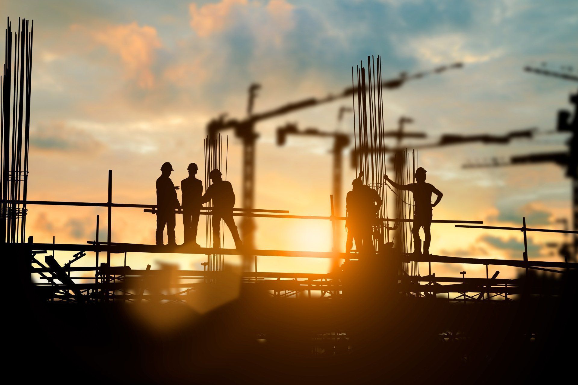 A group of construction workers are standing on top of a construction site at sunset.