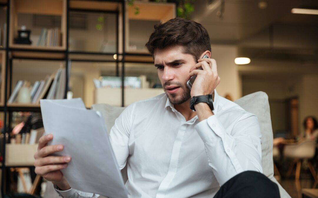 a man is sitting in a chair talking on a cell phone while holding a piece of paper