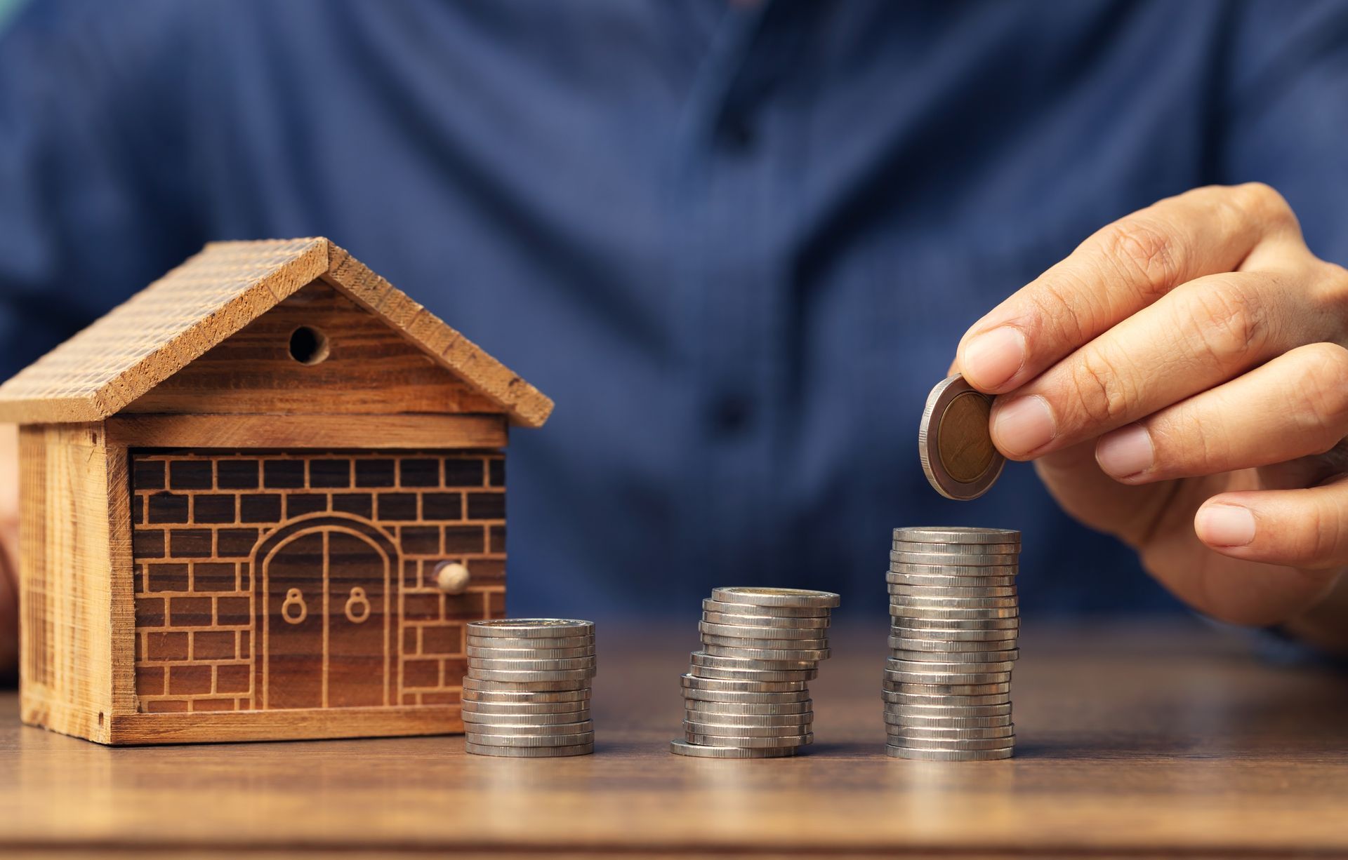A person is putting coins into stacks of coins next to a model house.