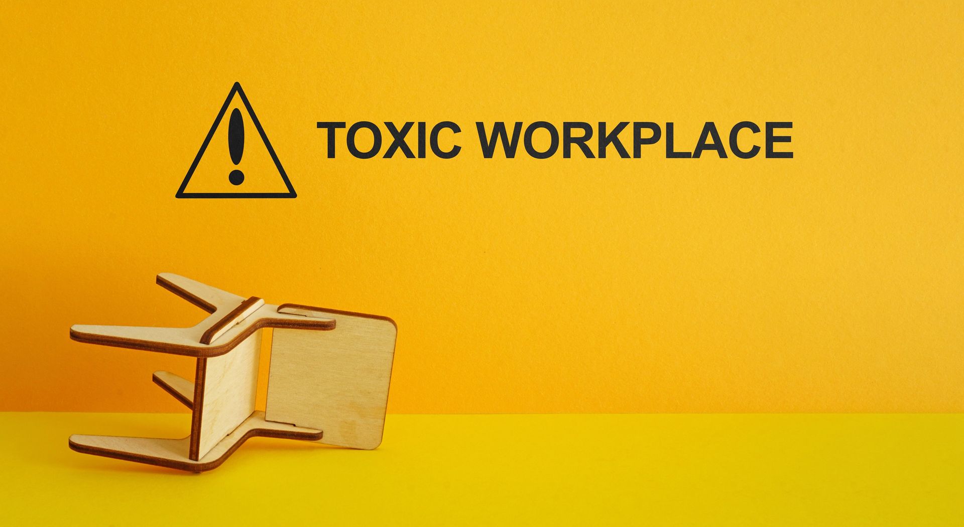 A wooden chair is laying on its side next to a sign that says toxic workplace.