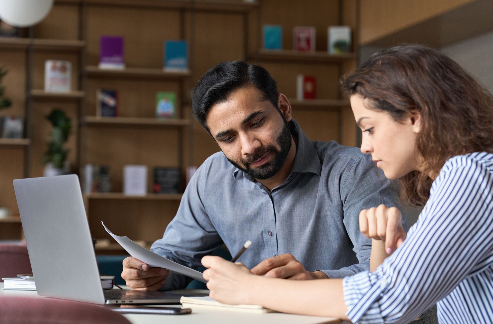 A man and a woman are sitting at a table looking at a laptop.