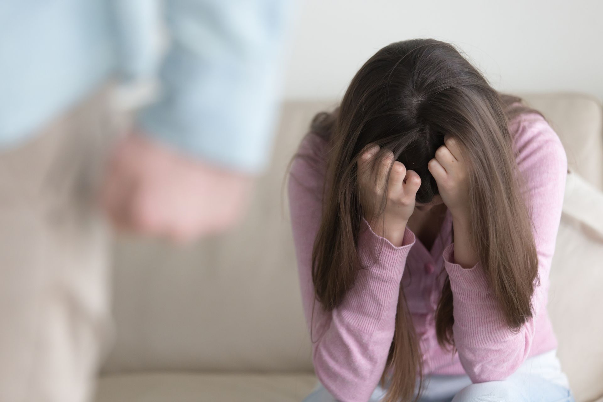 A woman is sitting on a couch with her head in her hands.