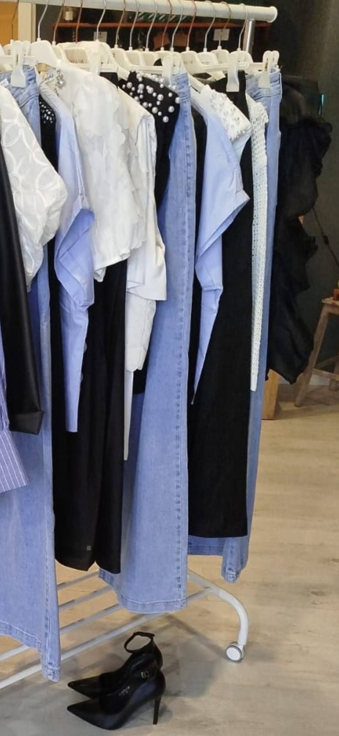 Appendiabiti con vari top e jeans. Tacchi alti neri sul pavimento.