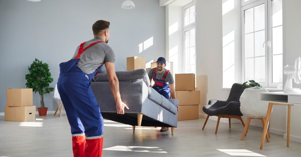 Two men are working together to lift up a couch. The couch is in a large room that is mostly empty.