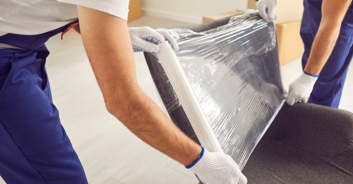 Two men are working together to cover an office chair in a protective, translucent film.
