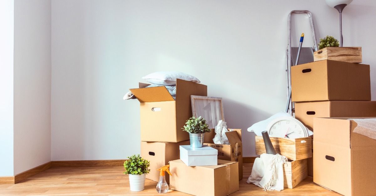 Several boxes are stacked in a corner of a room. The boxes are filled with items, and some boxes are not closed.