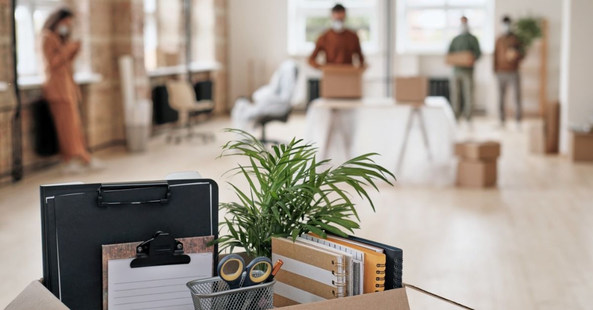 An office space is mostly empty of furniture. There are people in the background packing up.