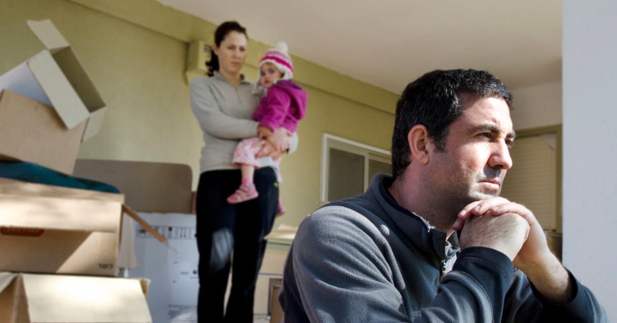 An older man is sitting in the foreground while a woman is holding a baby in the background.