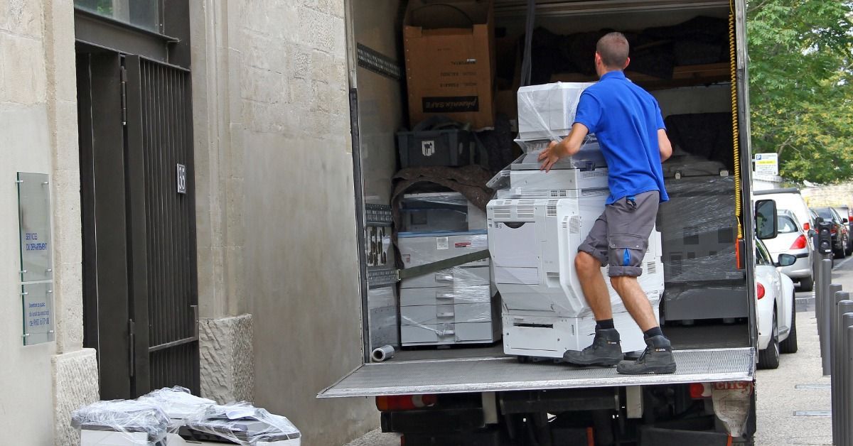 A man in a blue shirt is stacking boxes in a moving truck. The truck is already loaded with many boxes.