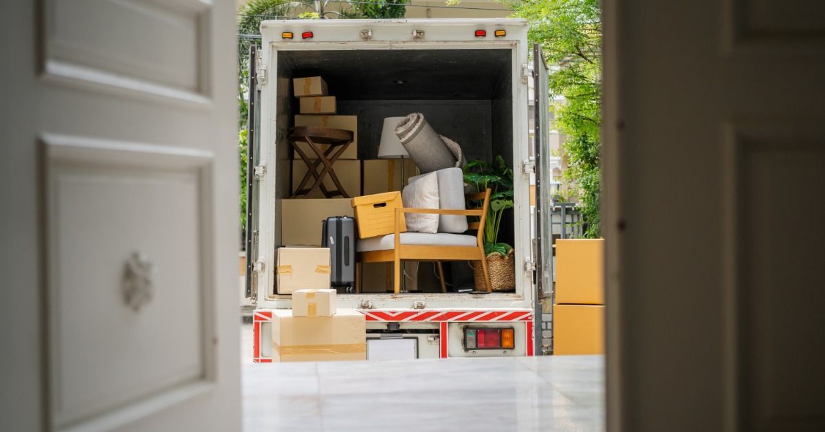 A door to a home is open, showing a box truck in the driveway with the back compartment open.
