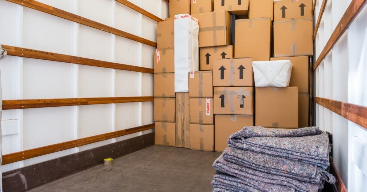 The storage compartment of a box truck. There is a wall of boxes pressed up against the far wall.