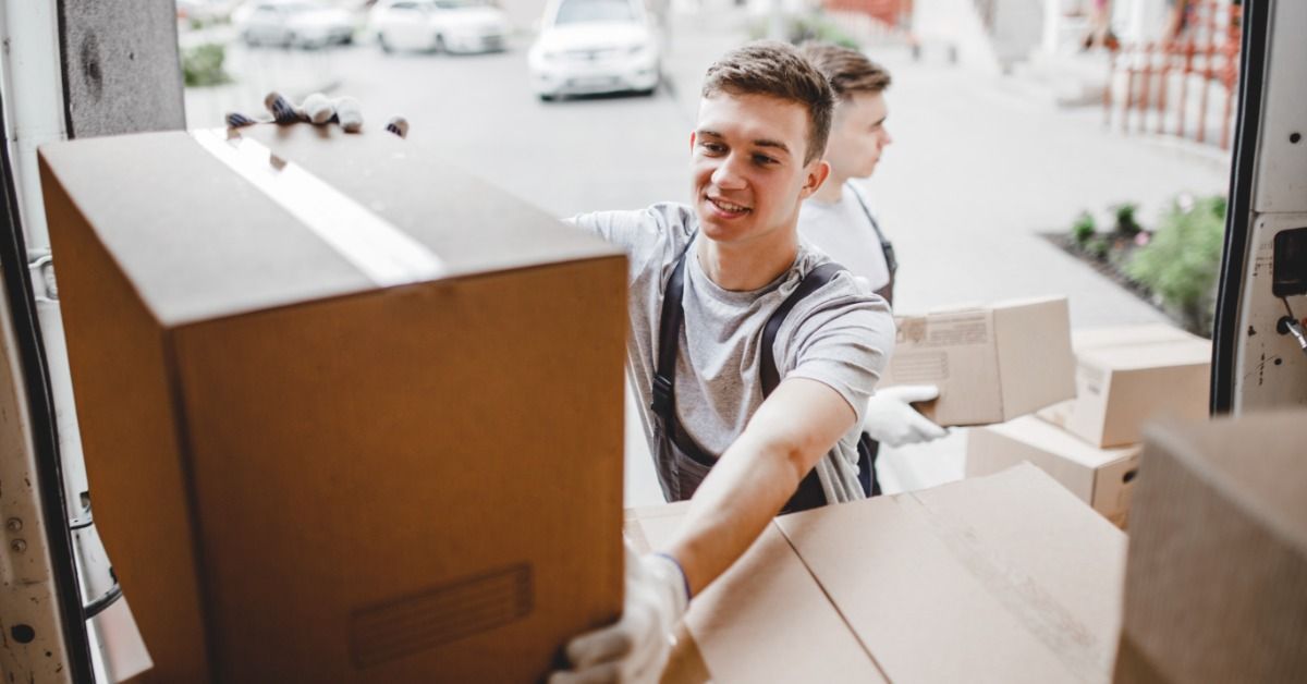 A man with short brown hair is placing a cardboard box into the back of a moving truck.