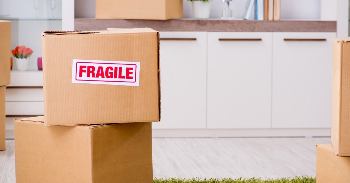 A cardboard box with a fragile sign on it is stacked on top of another cardboard box in a kitchen