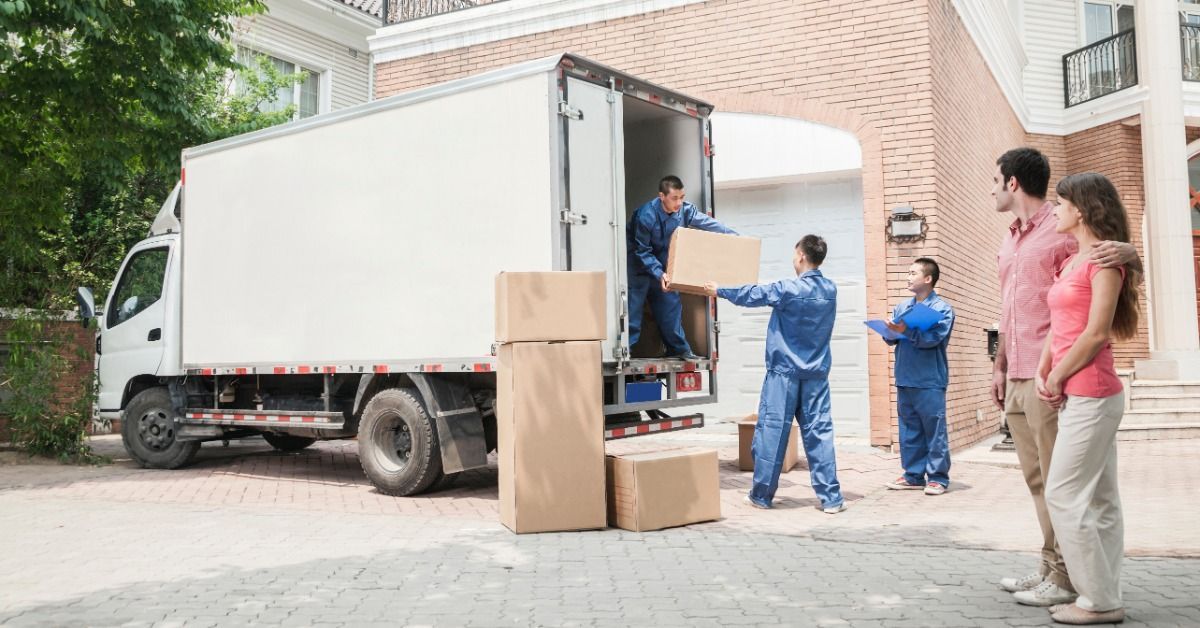 One man is standing in the back of a truck handing a box to another man that is standing outside the truck.