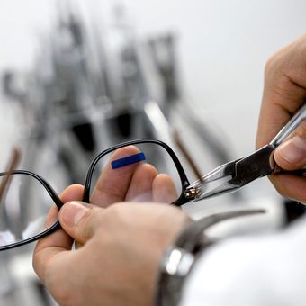 A person is holding a pair of scissors over a pair of glasses.