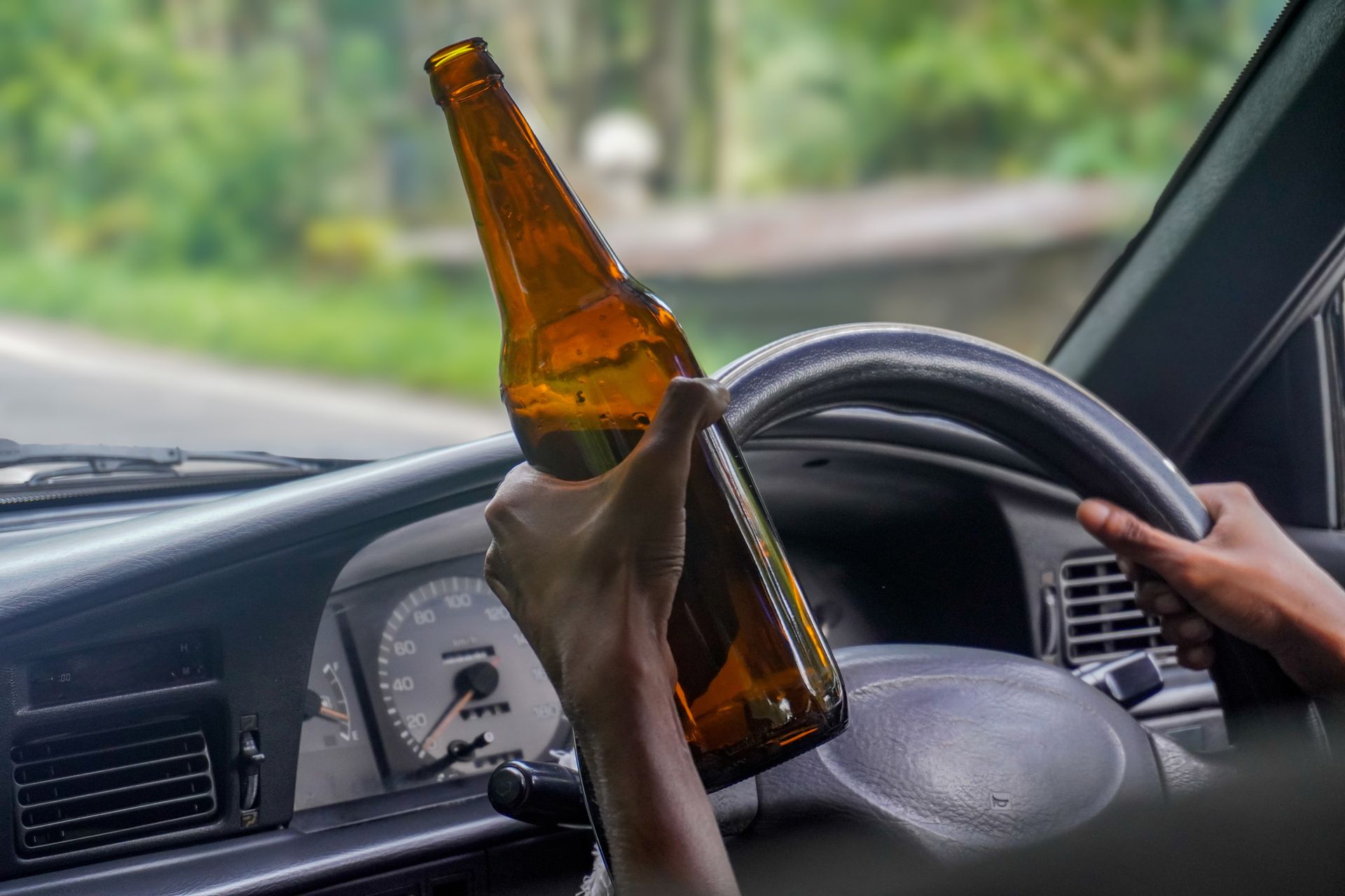 A person is holding a bottle of beer while driving a car.