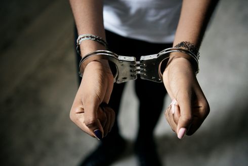 Handcuffed hands with bracelets hanging downward against a blurred gray background