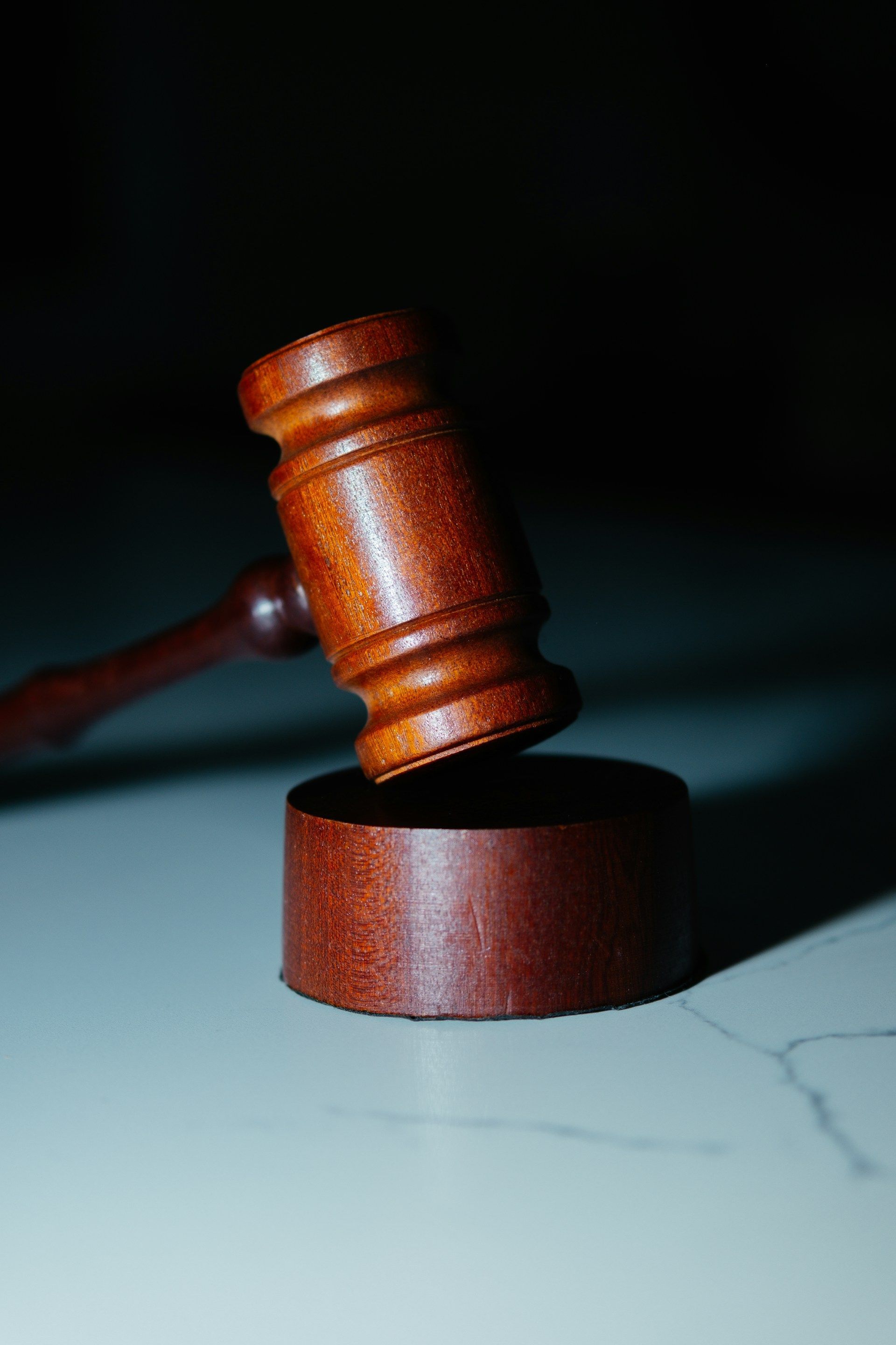 Wooden gavel resting on a round block, lit from above against a dark background.