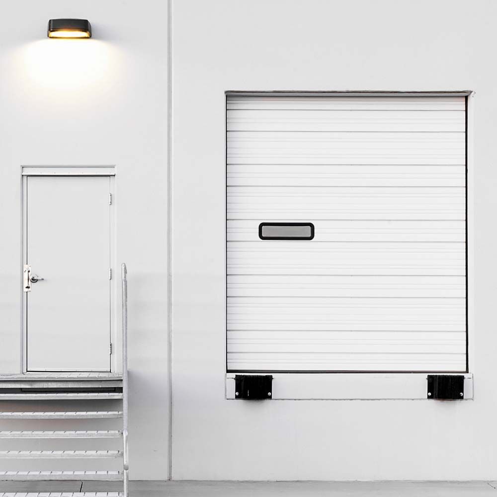 Exterior of a white warehouse with a loading dock door, a smaller door, and a wall light.