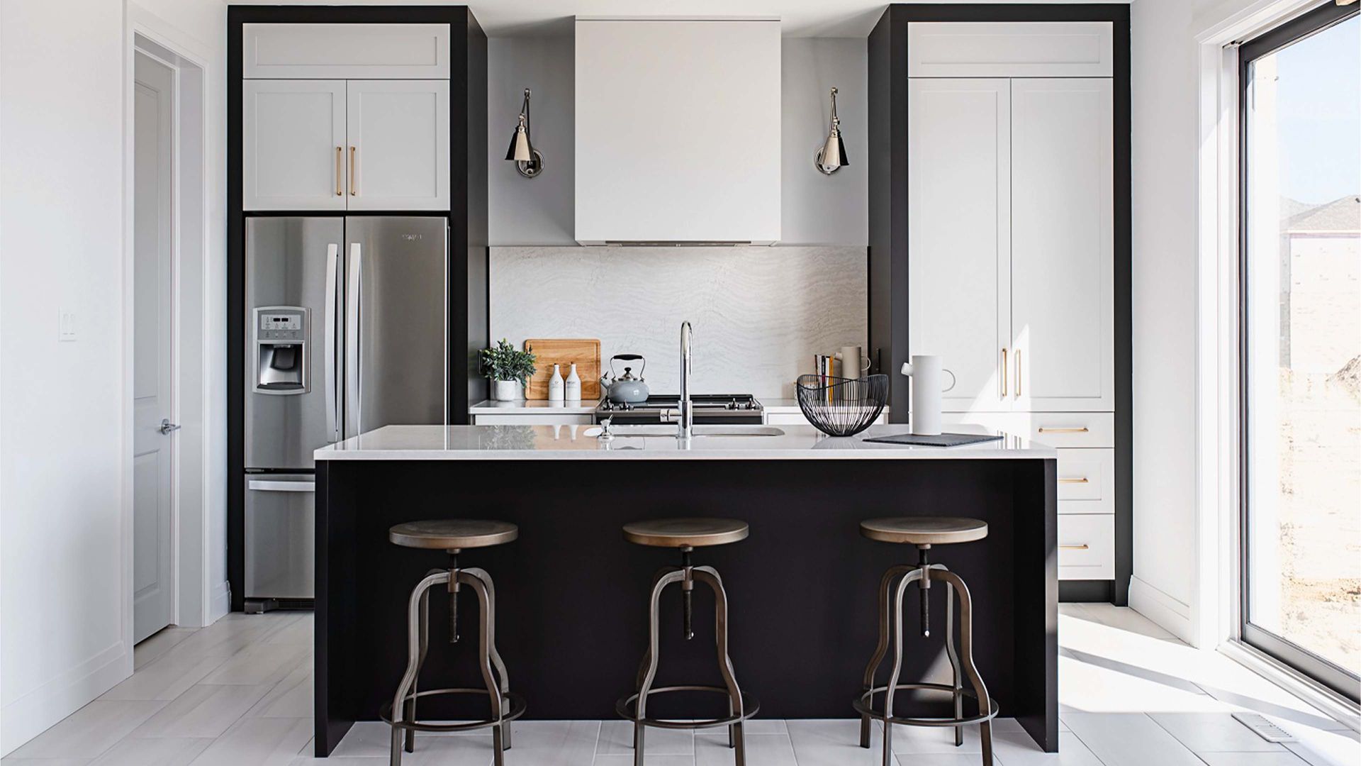 Modern kitchen with black and white cabinets, island with stools, and stainless steel appliances.