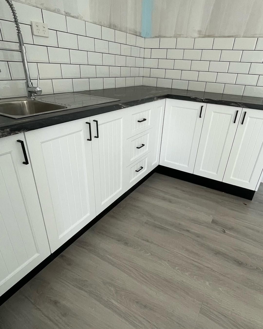 White kitchen cabinets with black countertops and hardware. Gray tile backsplash and flooring — Maken Kitchens & Cabinets in Chinderah, NSW