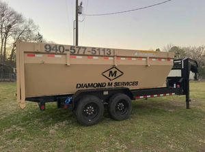 A tan dump trailer parked on grass, labeled with 