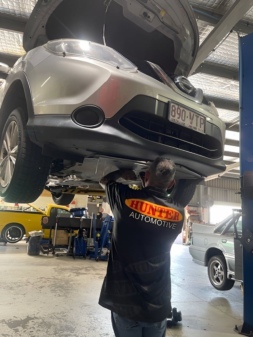 A Man Is Working On The Underside Of A Car In A Garage — Hunter Automotive In Bungalow, QLD