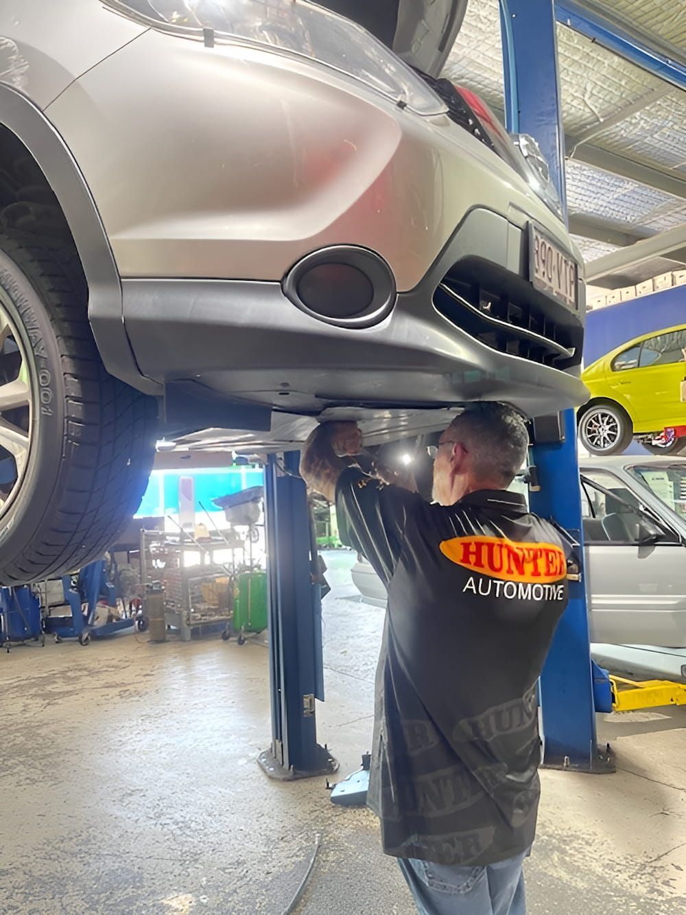A Man Is Working Under A Car On A Lift In A Garage — Hunter Automotive In Bungalow, QLD