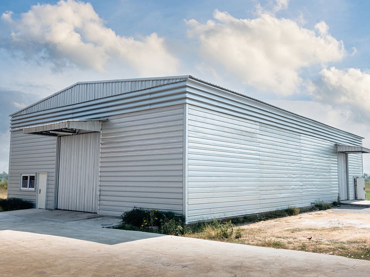 White corrugated metal warehouse with large sliding door under a partly cloudy sky